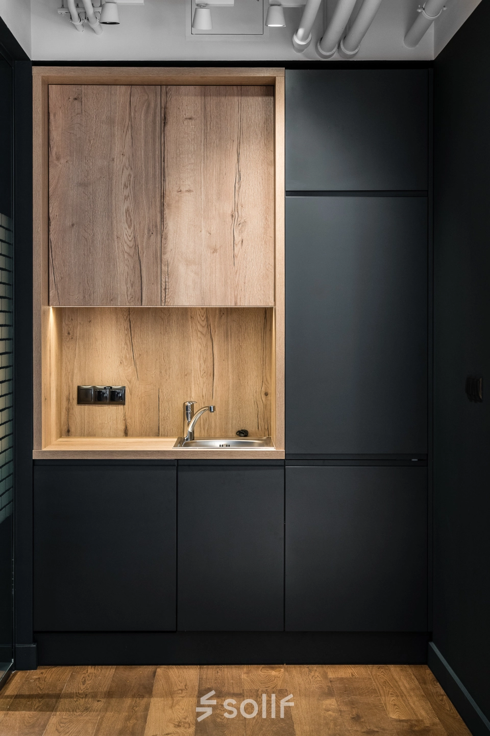 Modern office kitchen area with sleek black cabinets and wooden accents at Konstruktorska 11, Warsaw Mokotow. Ideal for office space rental.
