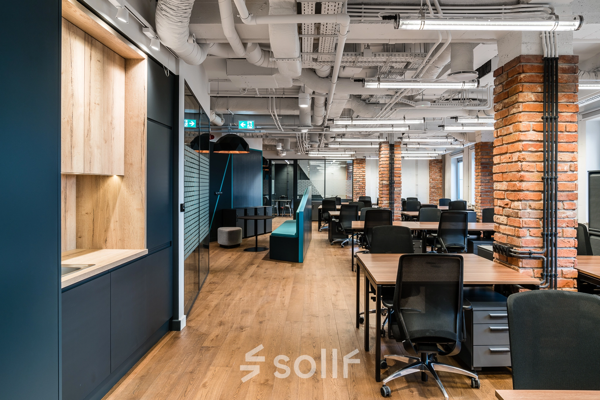 Modern office space with wooden floors, brick accent columns, and a mix of wood and metal furnishings at Konstruktorska 11, Warsaw Mokotow. Perfect for those looking for office space rental.