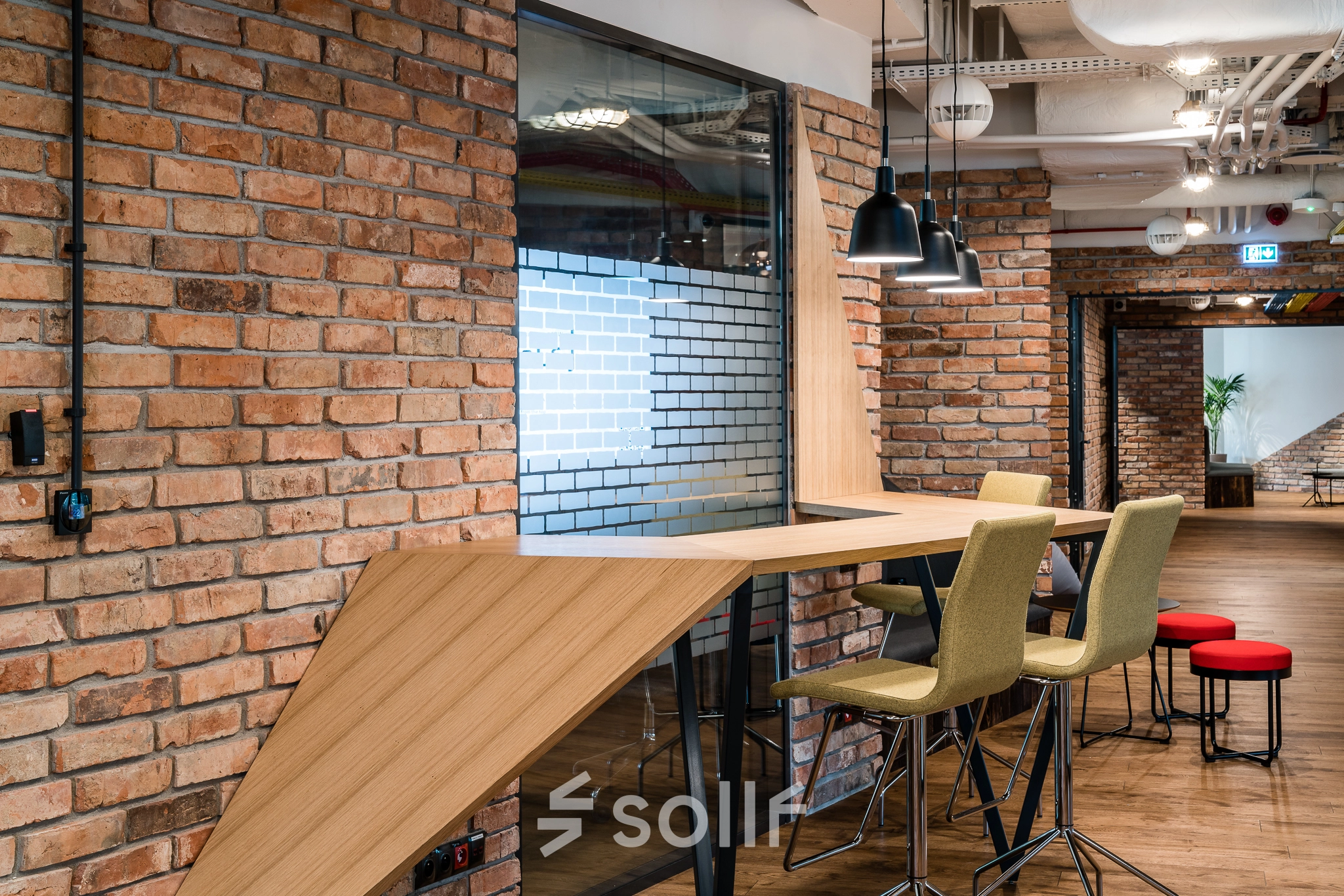 Modern workspace with high stools and wooden table in an office to rent, showcasing brick walls and contemporary lighting in Warsaw Mokotow.