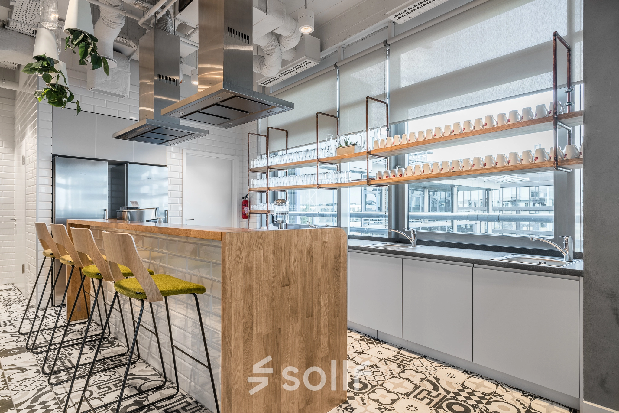 Modern office kitchen at Konstruktorska 11, Warsaw Mokotow, featuring a wooden island and bar stools. Ideal for office space rental.