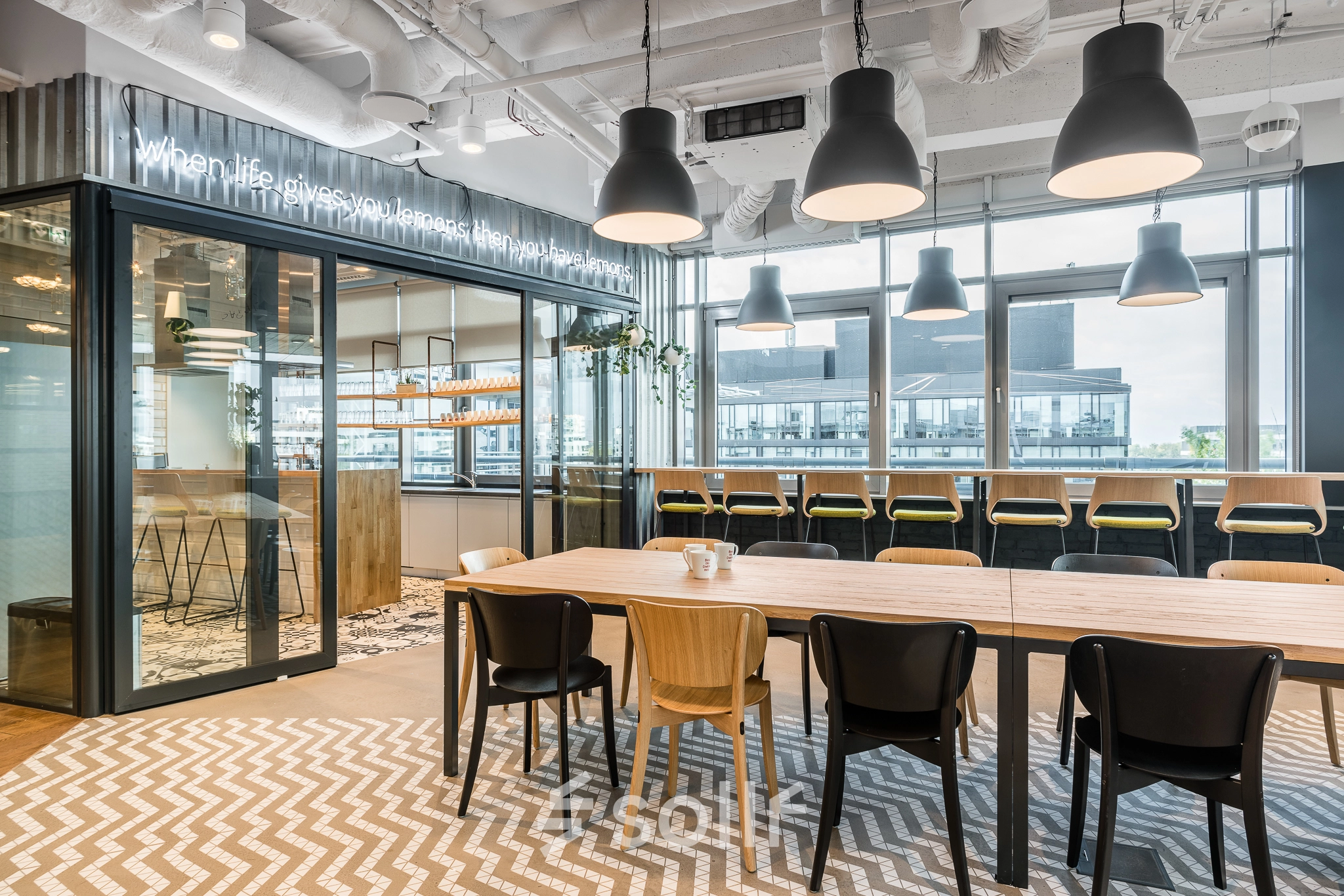 Modern furnished office space at Konstruktorska 11, Warsaw Mokotow with a communal table, high chairs by large windows, and contemporary lighting. Ideal office space rental for collaboration and creativity.