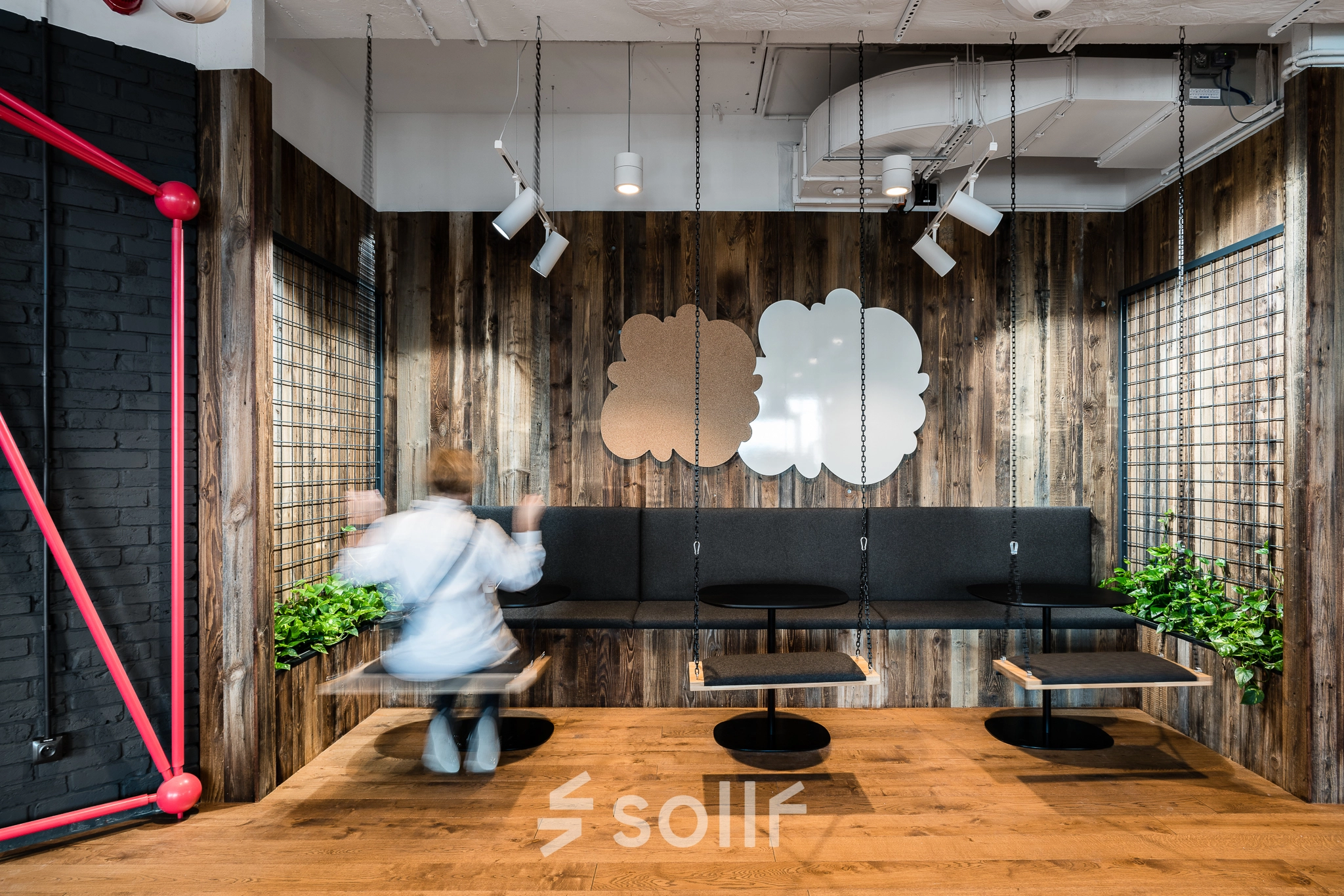 Modern office space with wooden walls at Konstruktorska 11, Warsaw Mokotow, featuring unique seating designs and plants, ideal for rent office space. A person is adjusting seating arrangements.