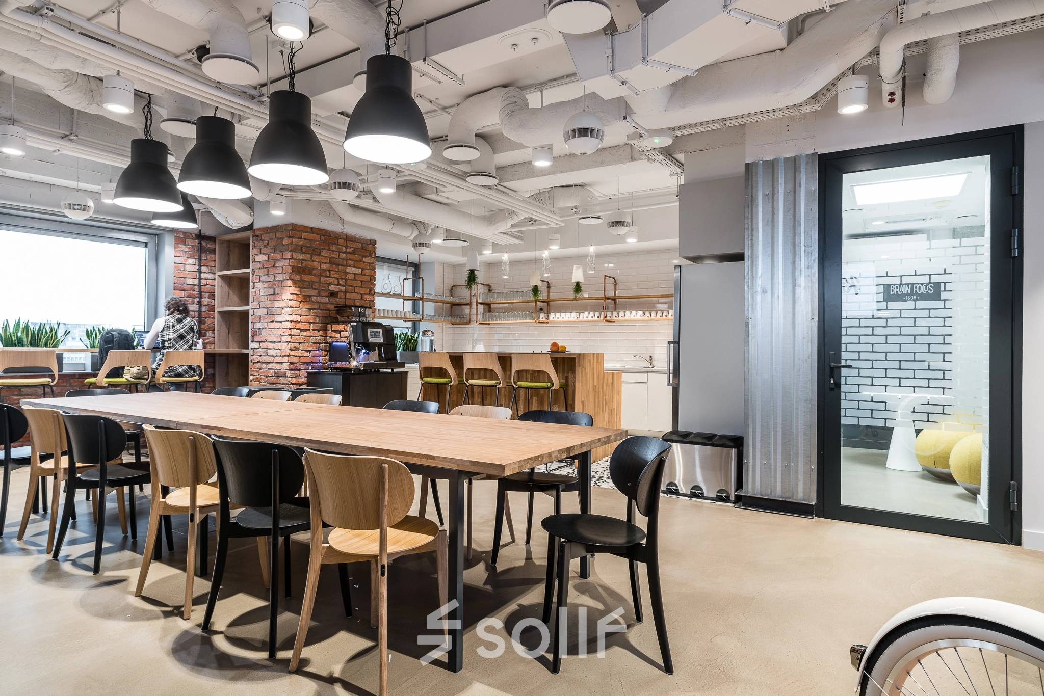 Modern office space at Konstruktorska 11, Warsaw Mokotow with a large wooden table, chairs, and a kitchenette area, ideal for office space rental.