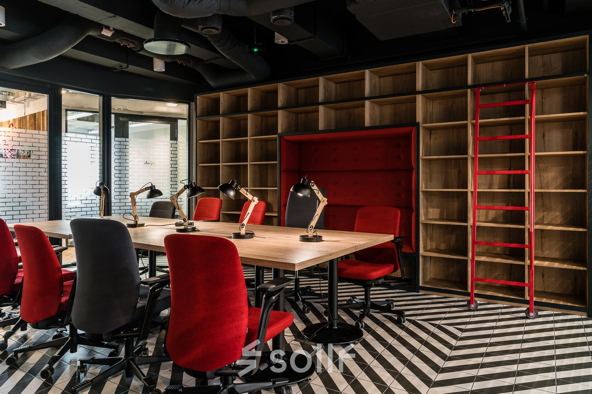 Furnished office space for rent at Konstruktorska 11, Warsaw Mokotow, featuring a stylish open floorplan with red chairs and industrial shelving.