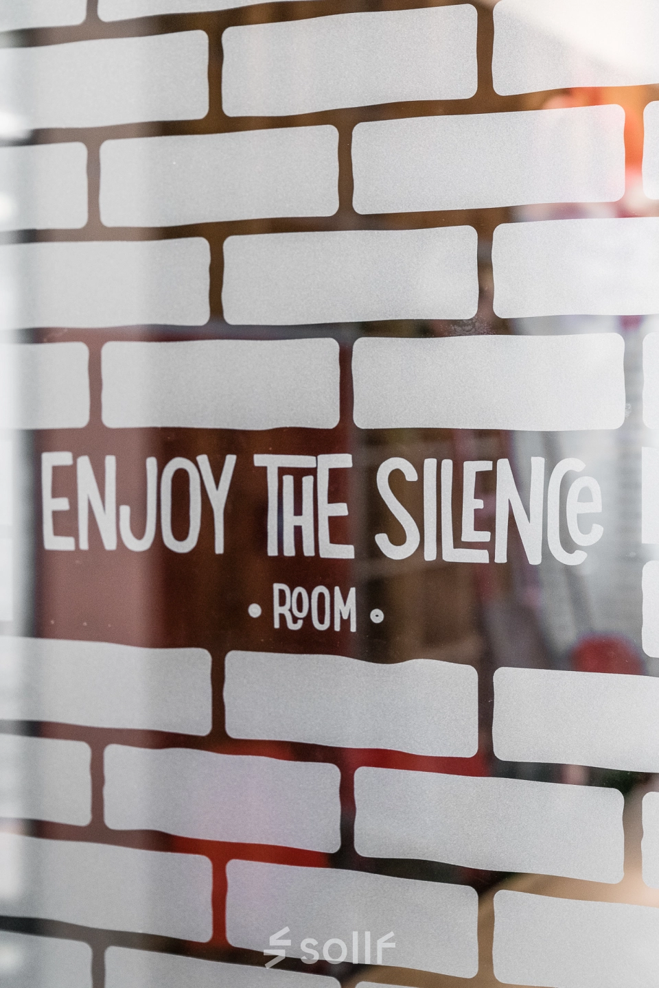 Close-up of a glass partition with brick pattern and 'Enjoy the Silence Room' text in an office space for rent at Konstruktorska 11, Warsaw Mokotow.