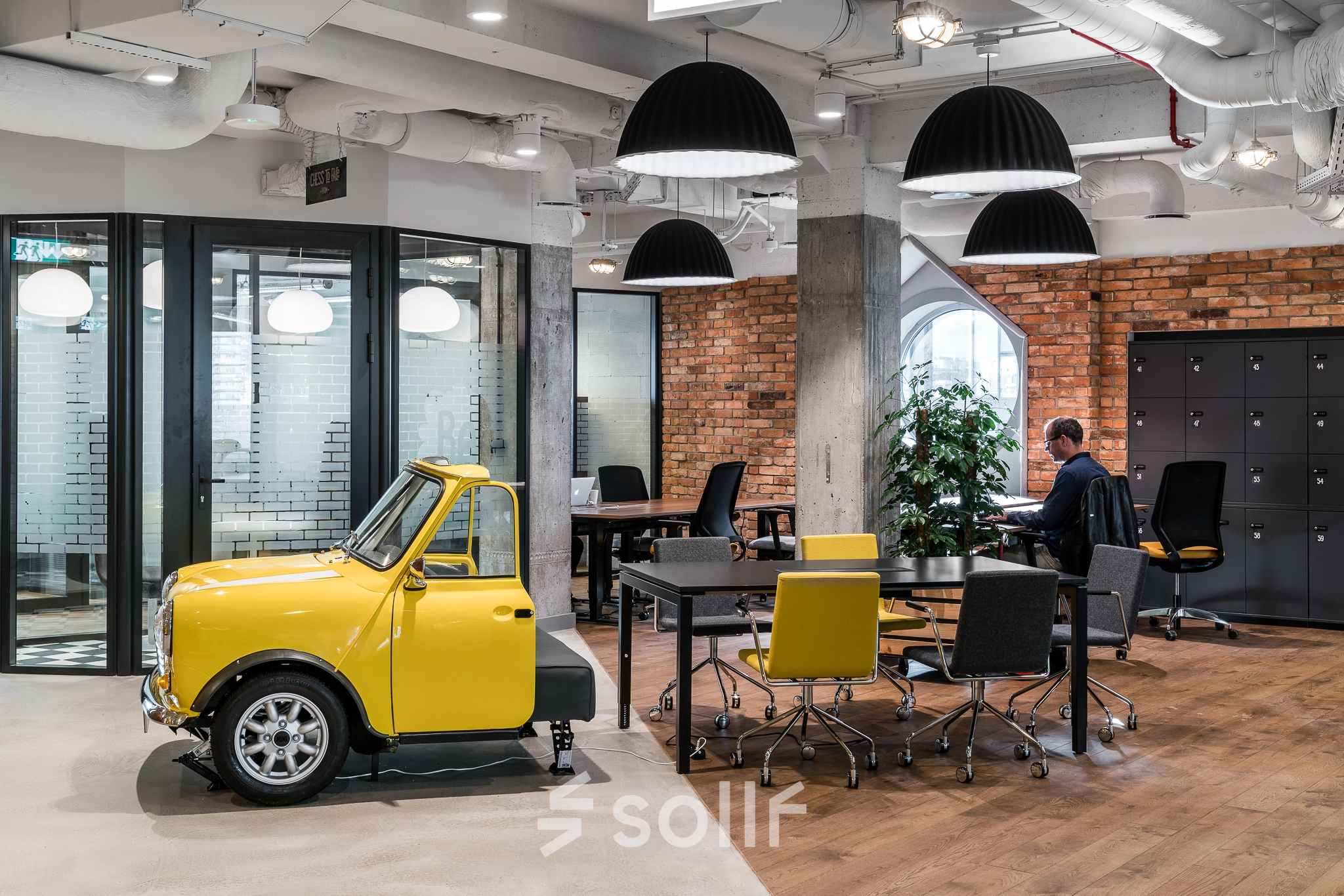 Office space rental at Konstruktorska 11, Warsaw Mokotow featuring a unique yellow car sculpture, modern workstations, and a person working at a desk.