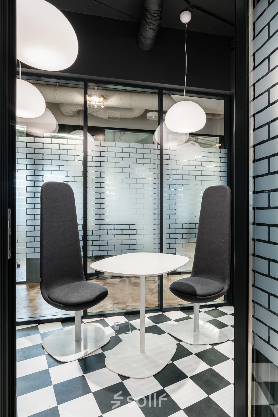Modern office space to rent at Konstruktorska 11, Warsaw Mokotow, featuring sleek black and white decor with high-backed chairs and a round table.