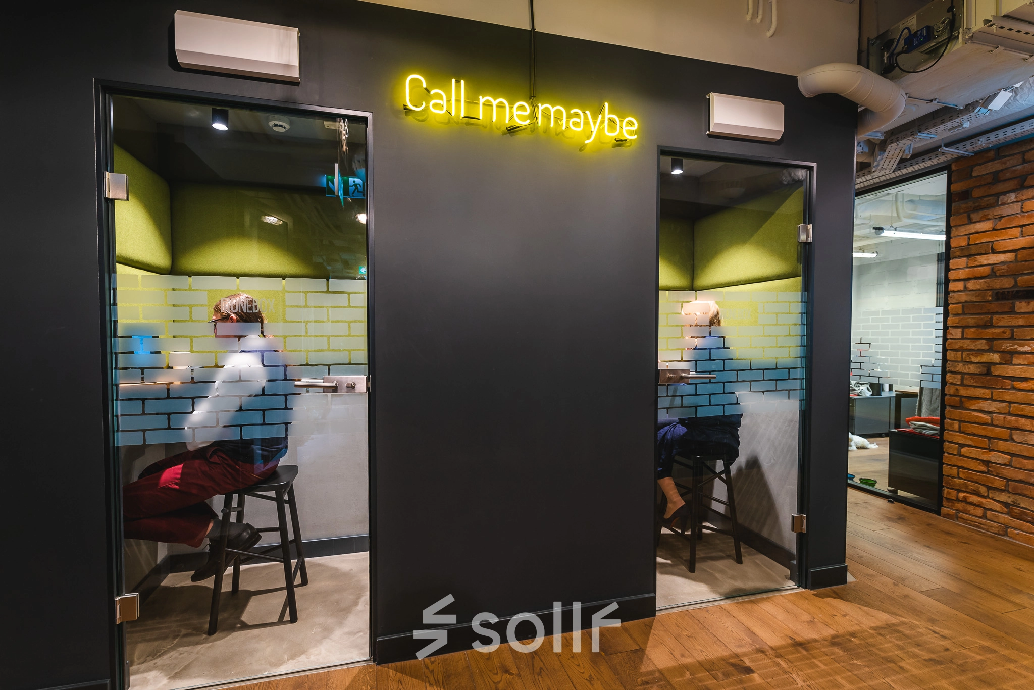 Two individuals work in private phone booths with glass doors in a modern office located at Konstruktorska 11, Warsaw Mokotow. Ideal office space rental for focused calls.