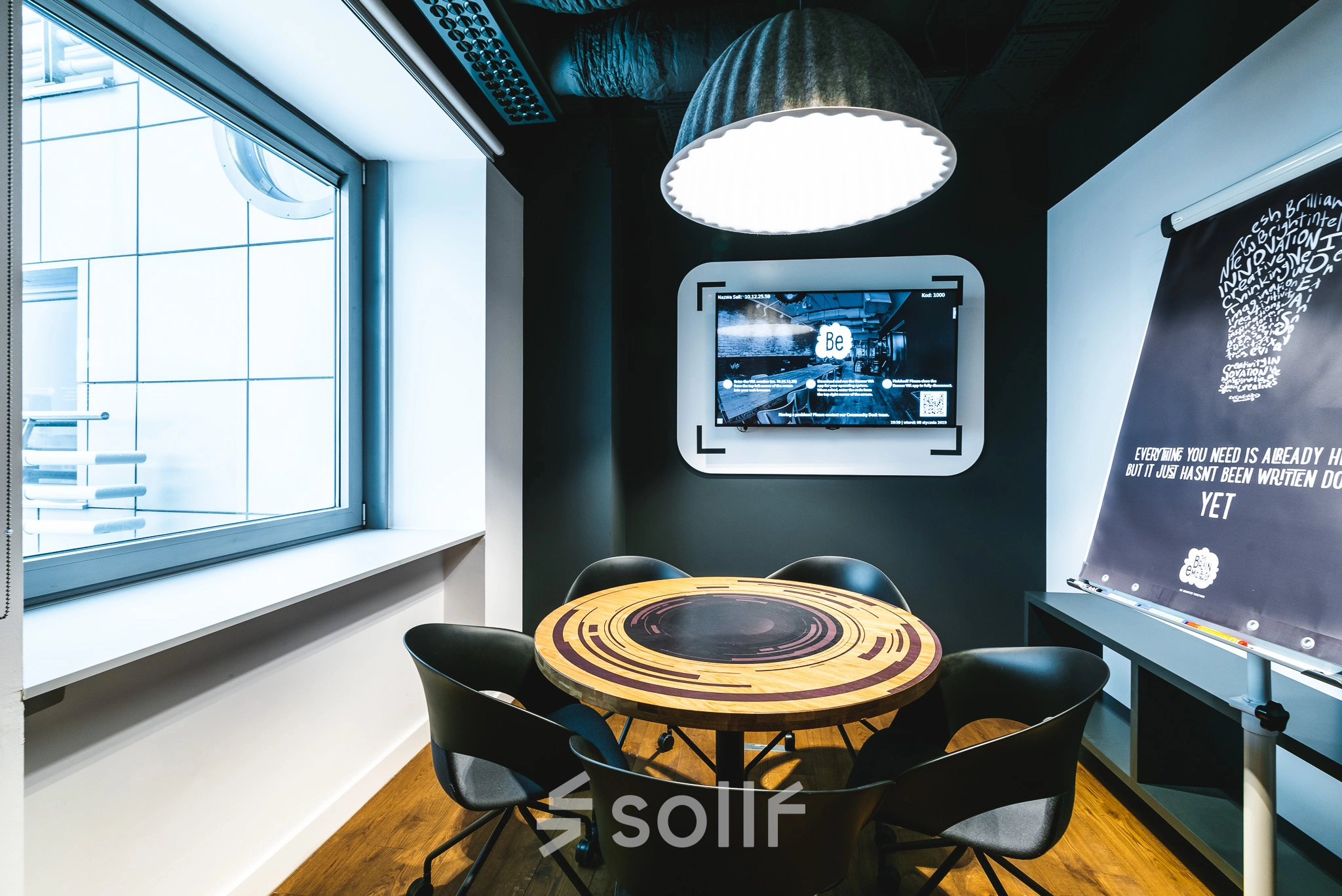 Modern furnished conference room at Konstruktorska 11, Warsaw Mokotow, featuring a round table, chairs, a wall-mounted screen, and a flip chart. Ideal office space rental for meetings.