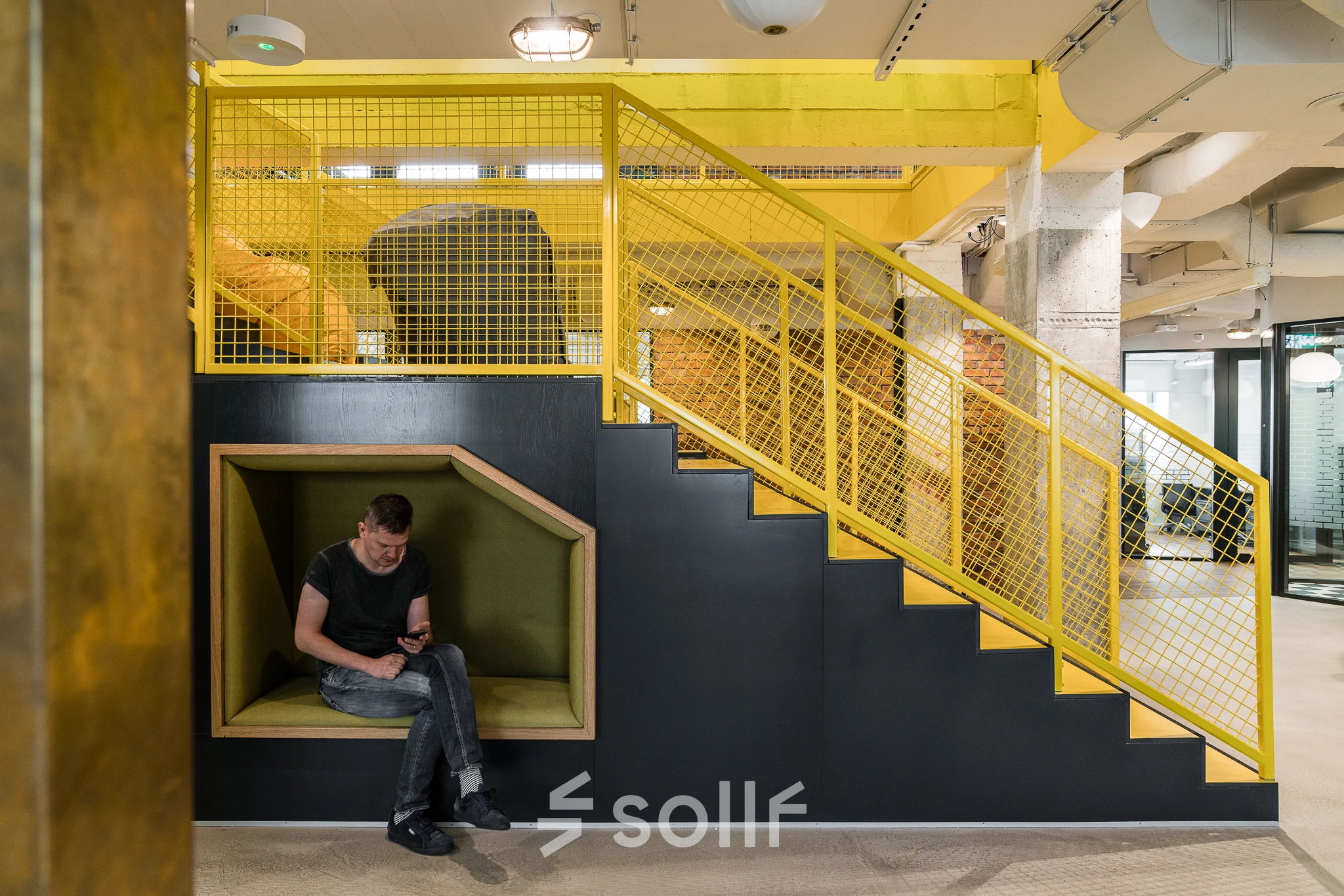 Modern office space at Konstruktorska 11, Warsaw Mokotow, featuring a vibrant yellow stair design with a cozy seating nook where a person is working on a laptop.