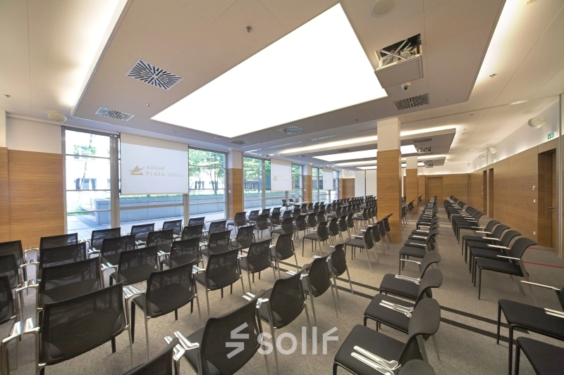 Spacious conference room with rows of black chairs, large windows, and modern lighting at Postępu 17A, Warsaw Mokotow for office space rental.