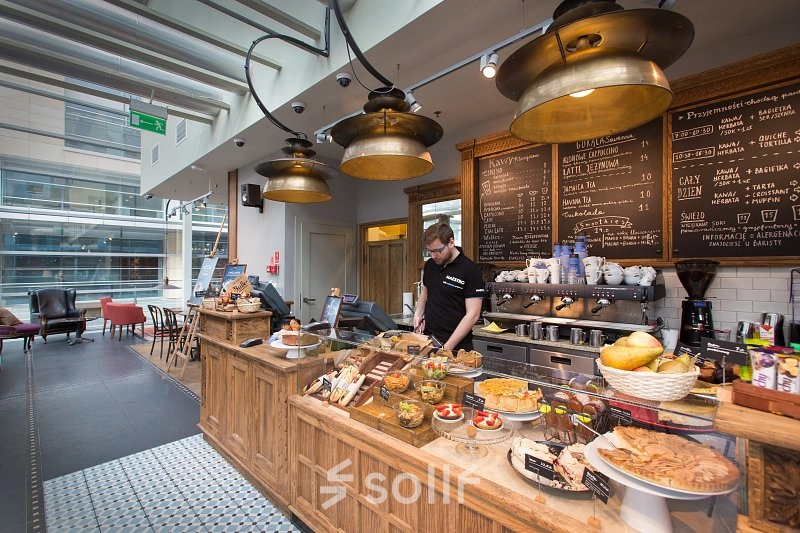 A cozy café area in an office space rental at Postępu 17A, Warsaw Mokotow, featuring a variety of pastries and a barista preparing drinks.