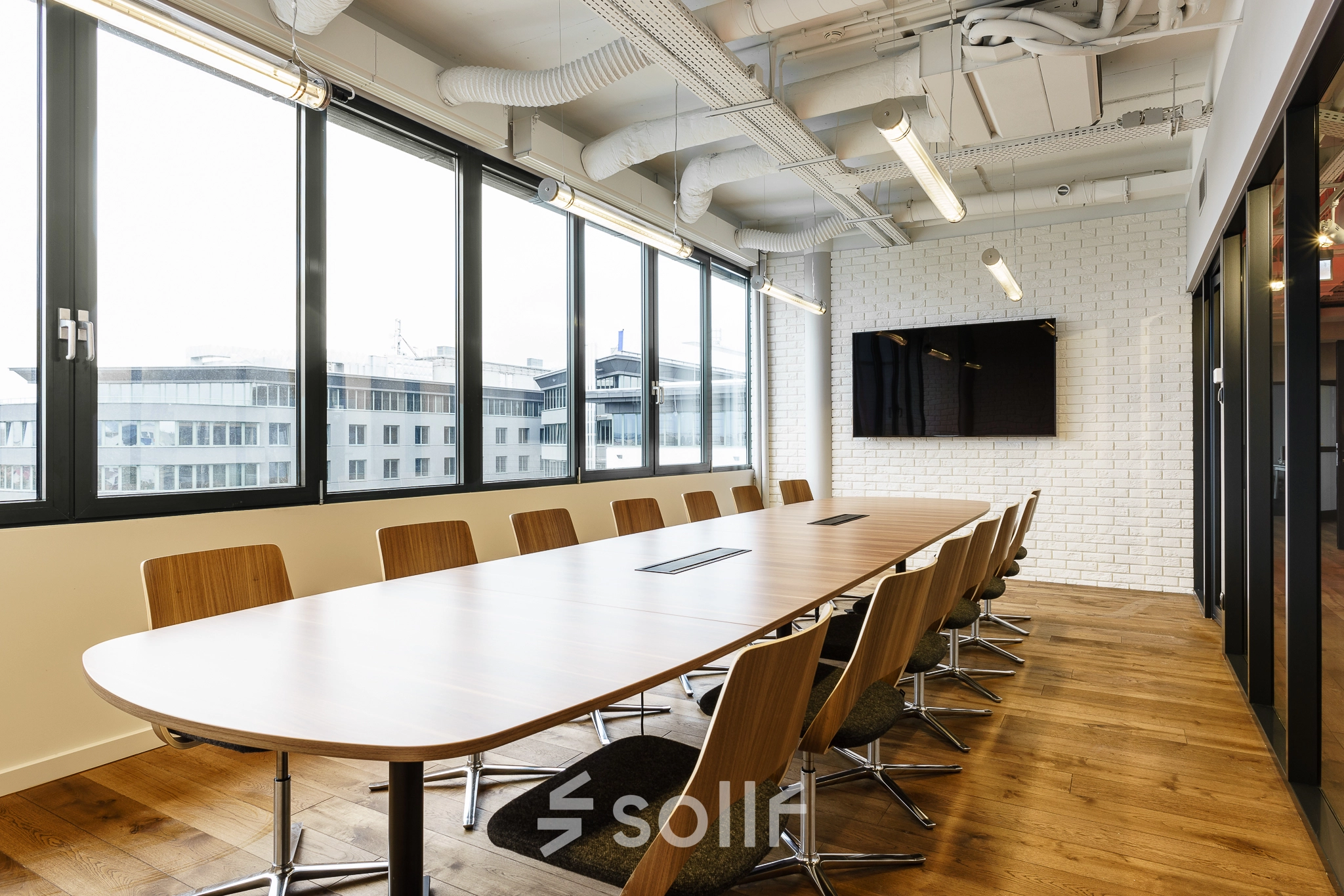 Spacious conference room in Warsaw Ochota with a long wooden table, modern chairs, and a large screen, ideal for office space rental meetings.
