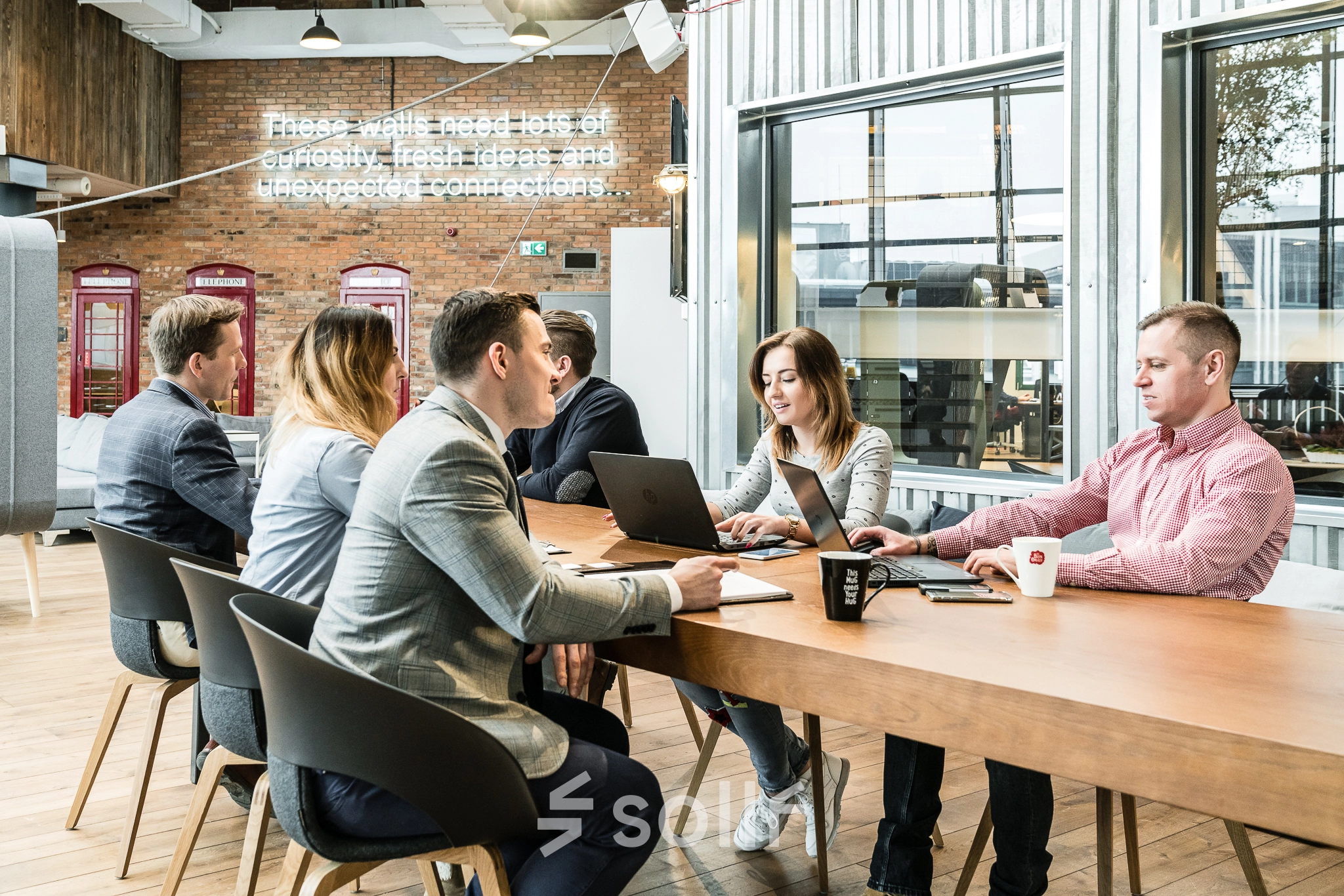 Group of people engaged in a meeting around a large wooden table in a modern office space at Al. Jerozolimskie 181B, Warsaw Ochota, available for office space rental.