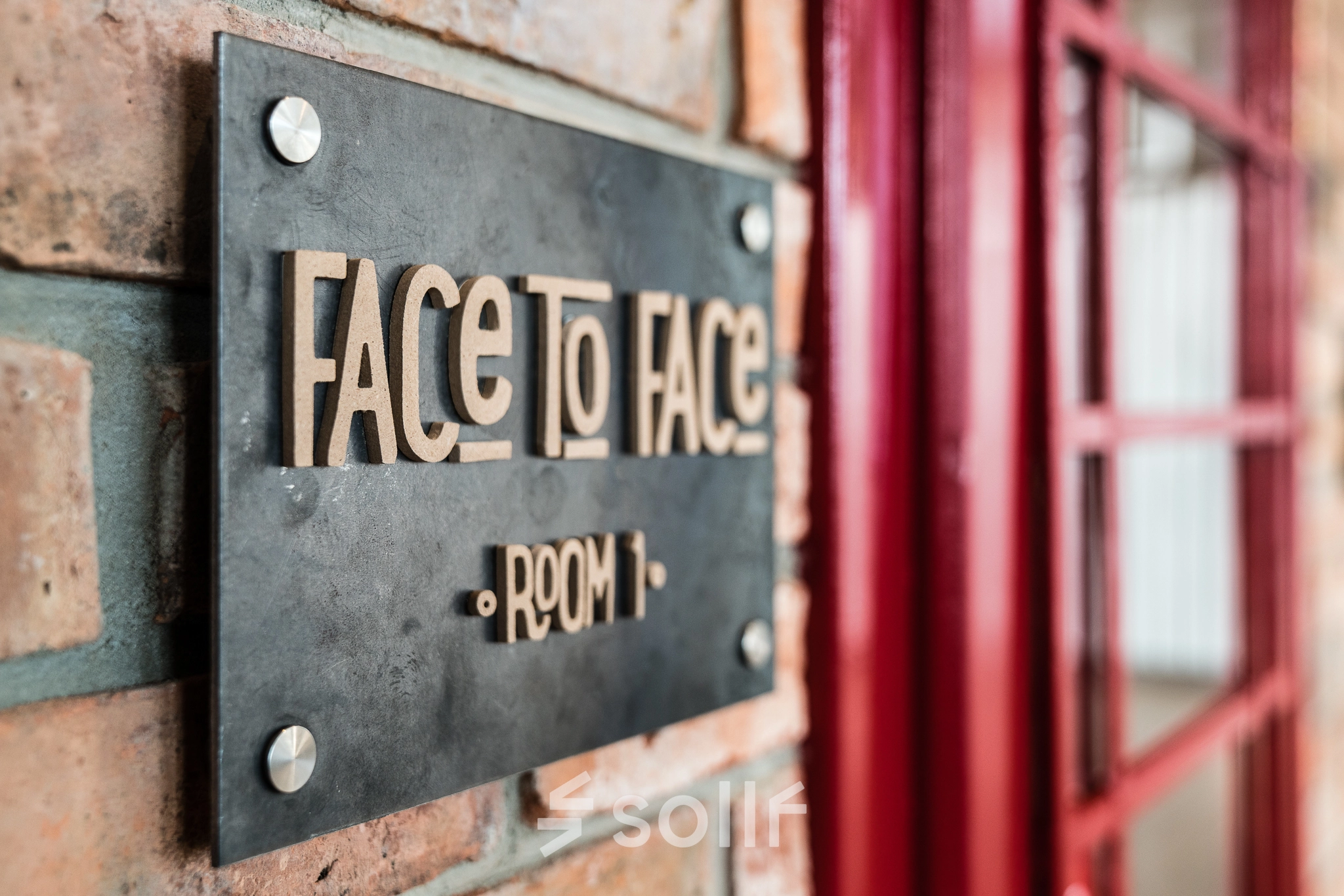 Close-up of a sign reading 'Face to Face Room 1' on a brick wall at the office to rent on Al. Jerozolimskie 181B, Warsaw Ochota.