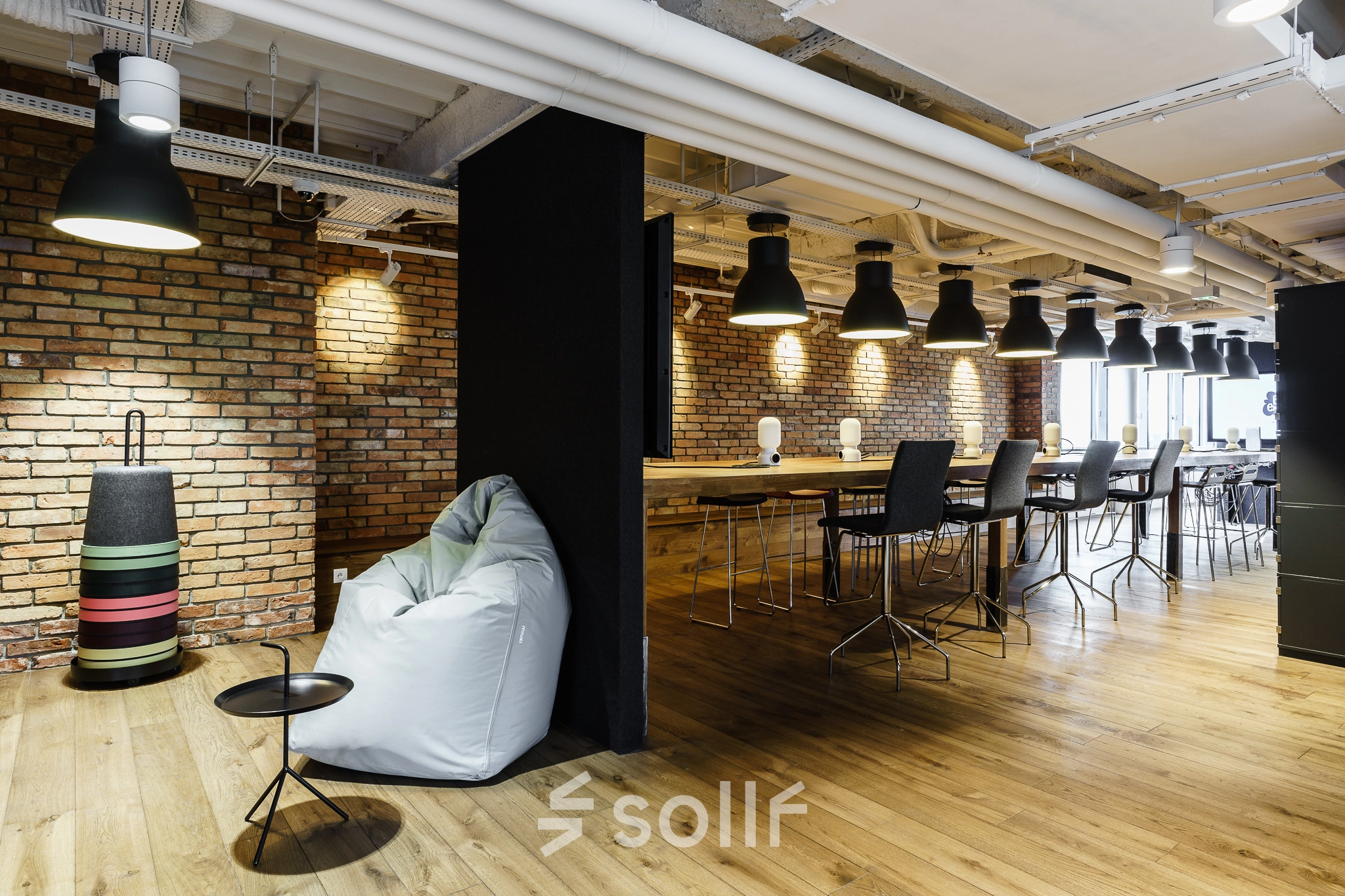 Modern office space with brick walls, wooden flooring, high ceilings, and a mix of seating options, perfect for open-floor plan office space rental.