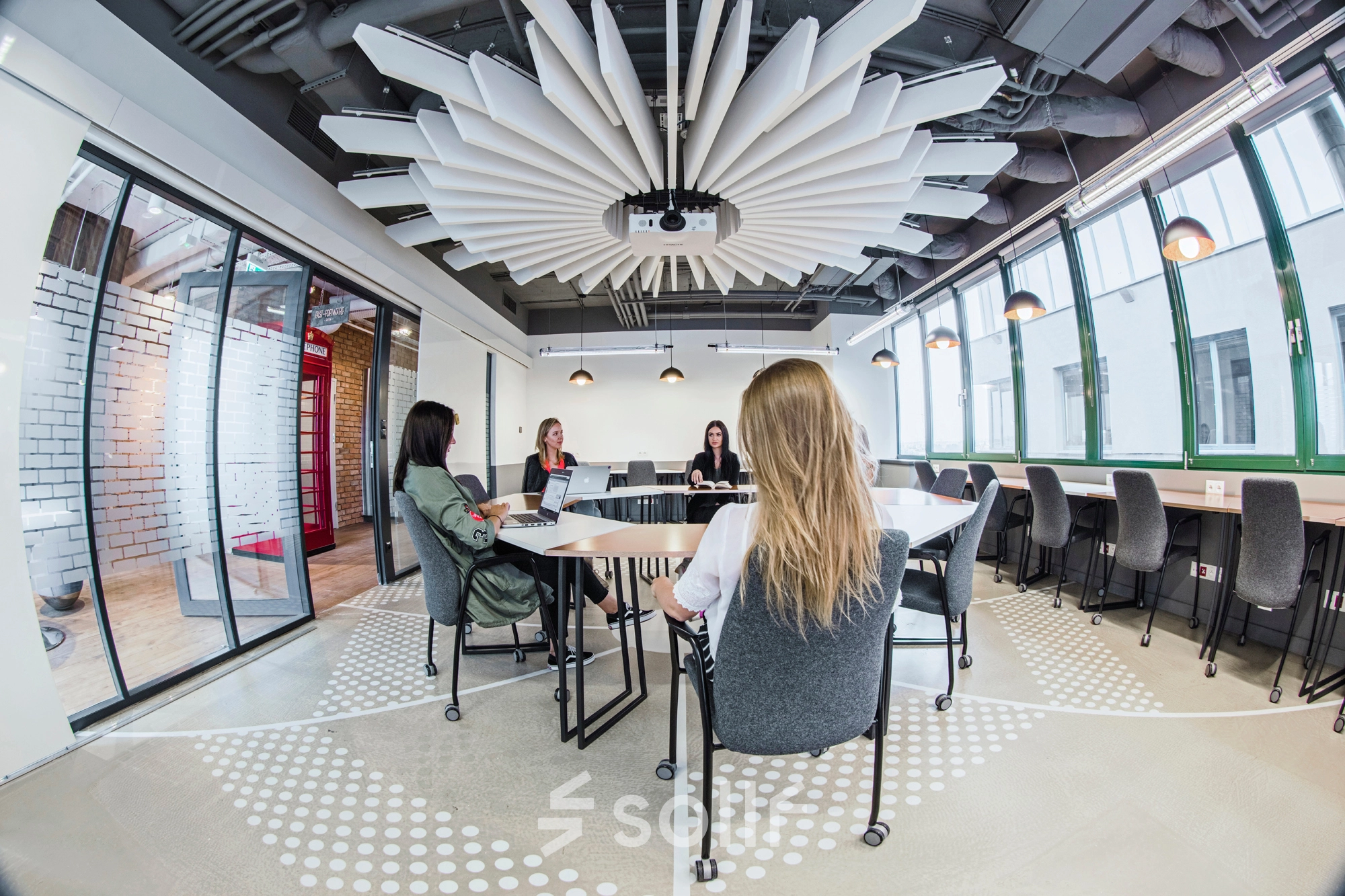 Modern office space in Warsaw Ochota at Al. Jerozolimskie 181B featuring a conference area with tables where people are engaged in business discussions, ideal for office space rental.