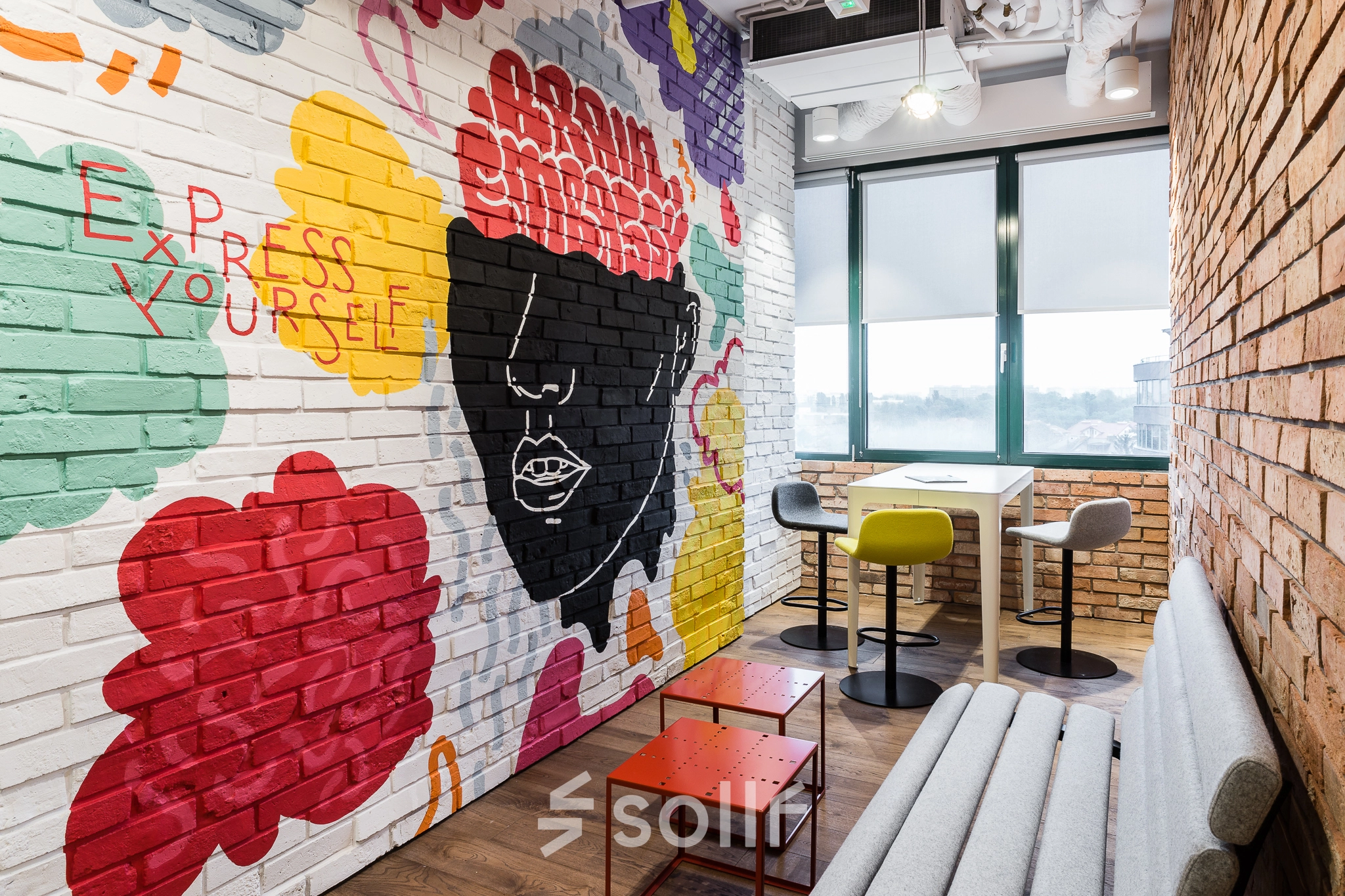 A creatively designed office space in Warsaw Ochota with vibrant graffiti art on the walls, cozy seating, and a view from the window. Ideal for office space rental.