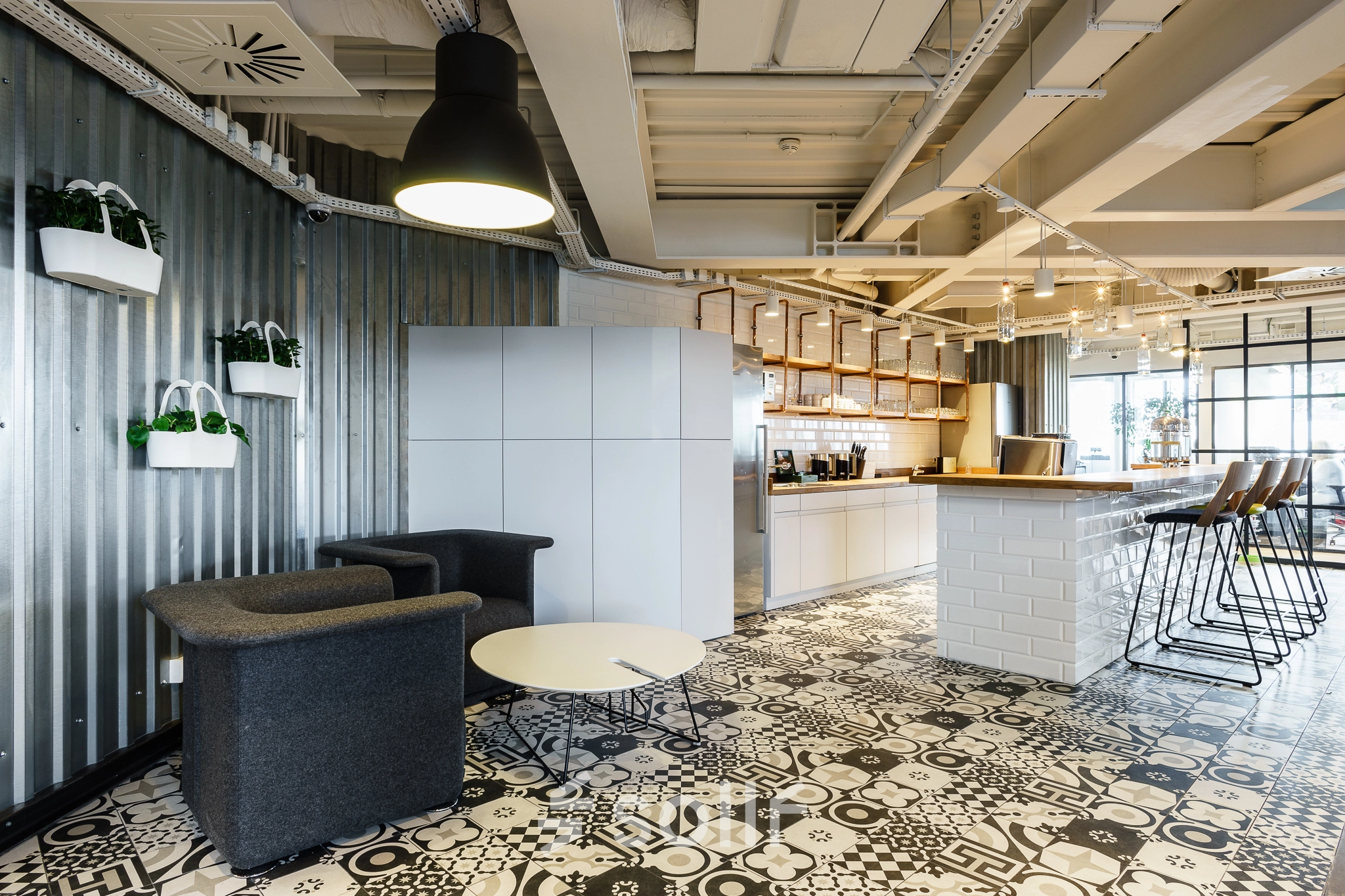 Modern office space for rent in Warsaw Ochota, featuring a stylish lounge area with seating and a coffee bar under industrial lighting.
