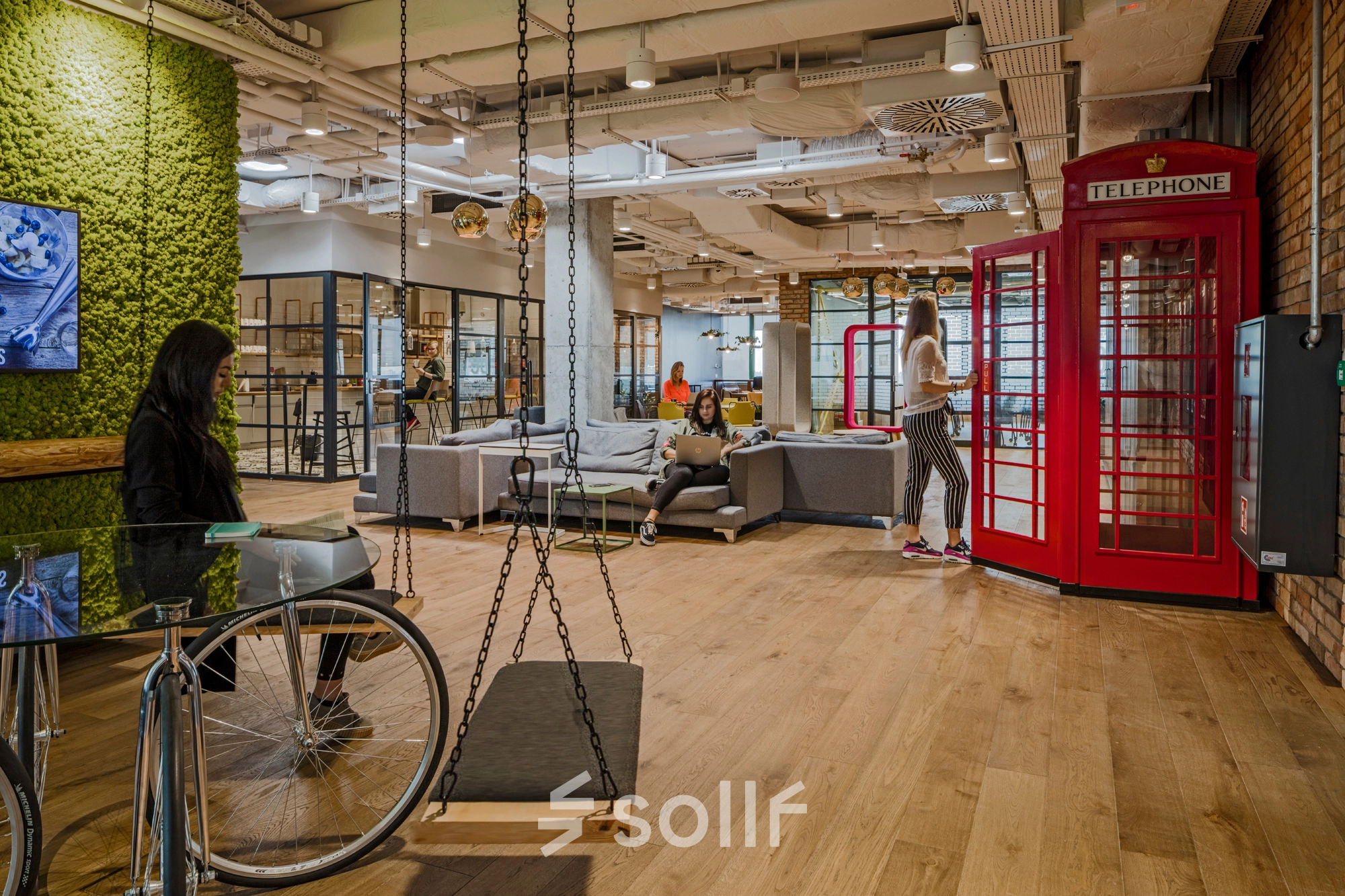 Vibrant and modern office space for rent with unique decor, including red phone booths and flexible seating areas, at Al. Jerozolimskie 181B, Warsaw Ochota. People engage in various business activities.
