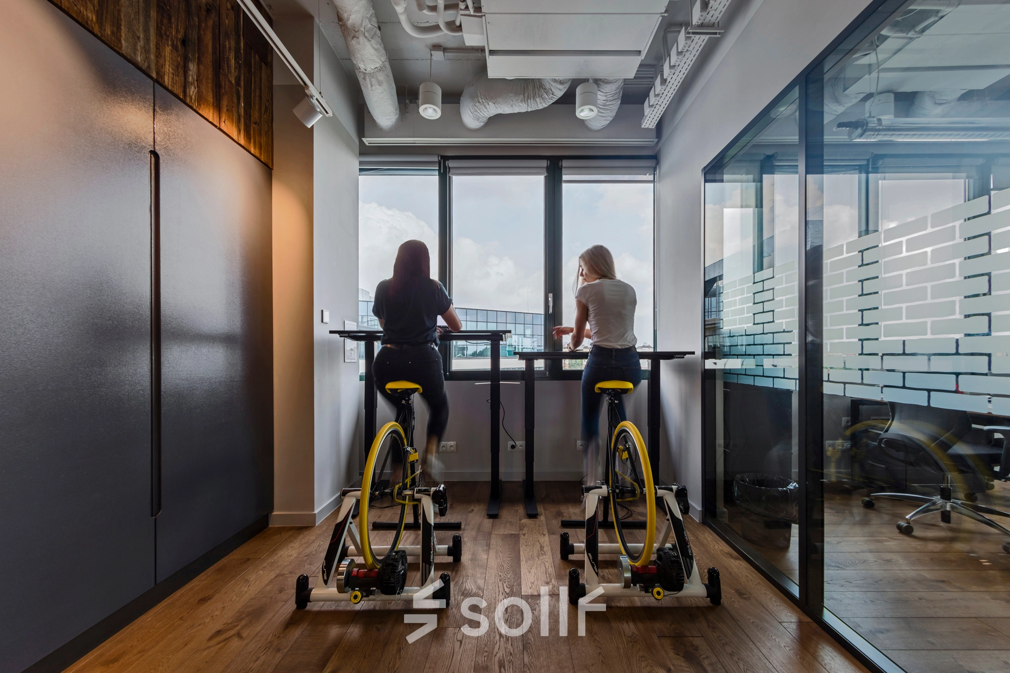 Two people engage in brainstorming while cycling at a standing desk in an office space rental at Al. Jerozolimskie 181B, Warsaw Ochota.