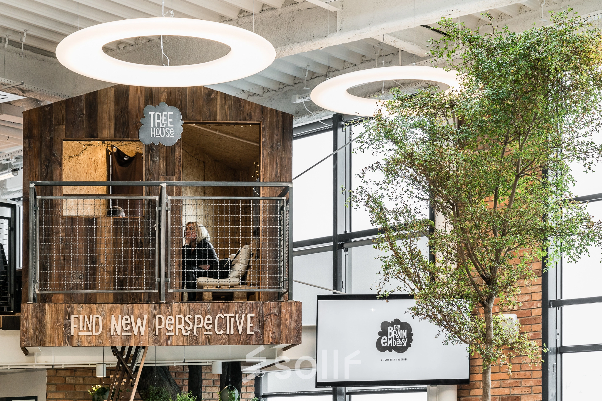 Unique treehouse-themed workspace in Warsaw Ochota with a person working on a laptop, surrounded by modern design elements and greenery, ideal for those seeking office space rental opportunities.