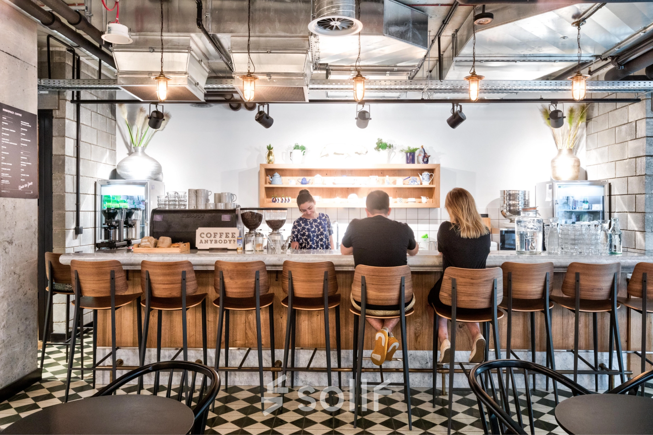 A modern office lounge at Koszykowa 61, Warsaw Śródmieście, featuring a bar counter with three people engaged in conversation, ideal for casual meetings and office space rental.