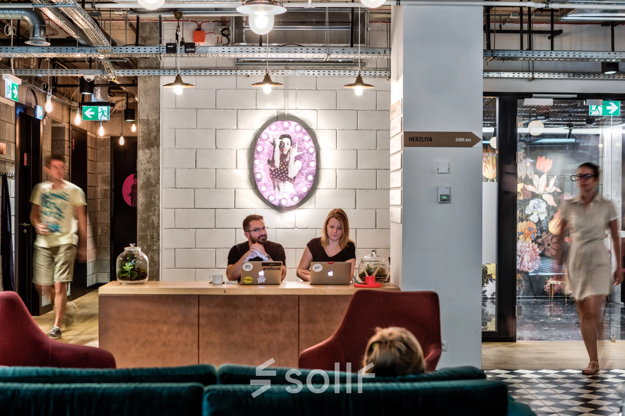 A modern, furnished office space in Warsaw Śródmieście with two people working on laptops at a reception desk, highlighting an inviting office space rental option.