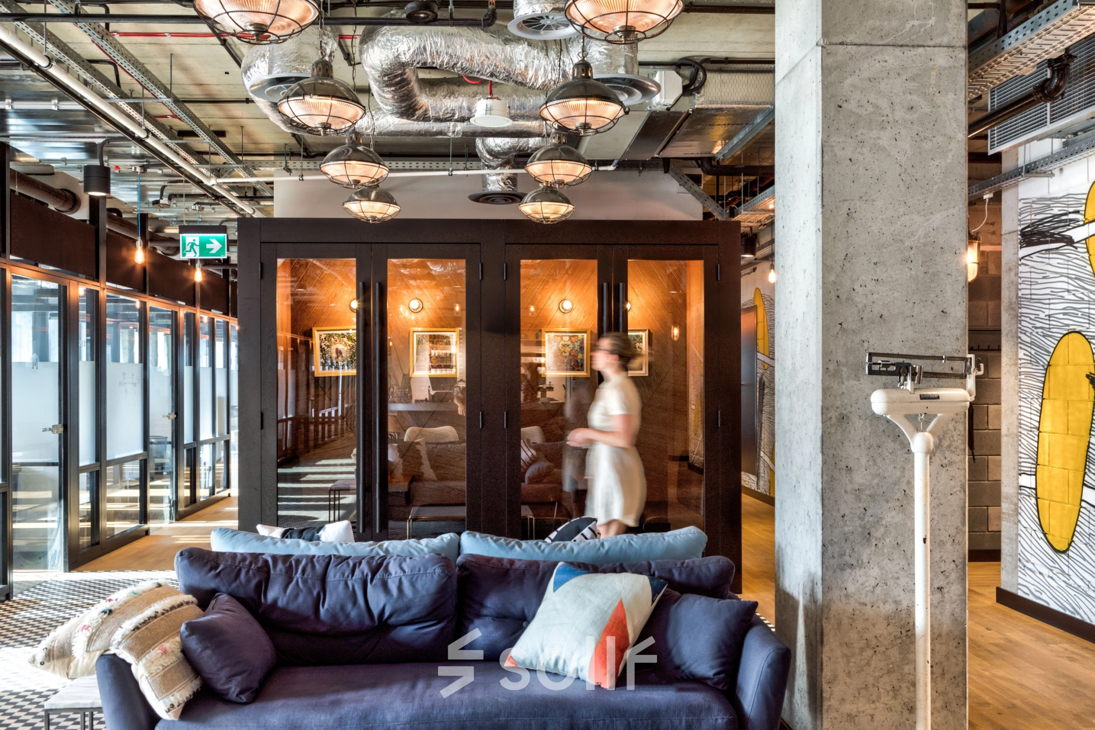 Stylish office space with modern industrial design, featuring comfortable seating and glass-walled meeting rooms at Koszykowa 61 in Warsaw, ideal for office space rental.
