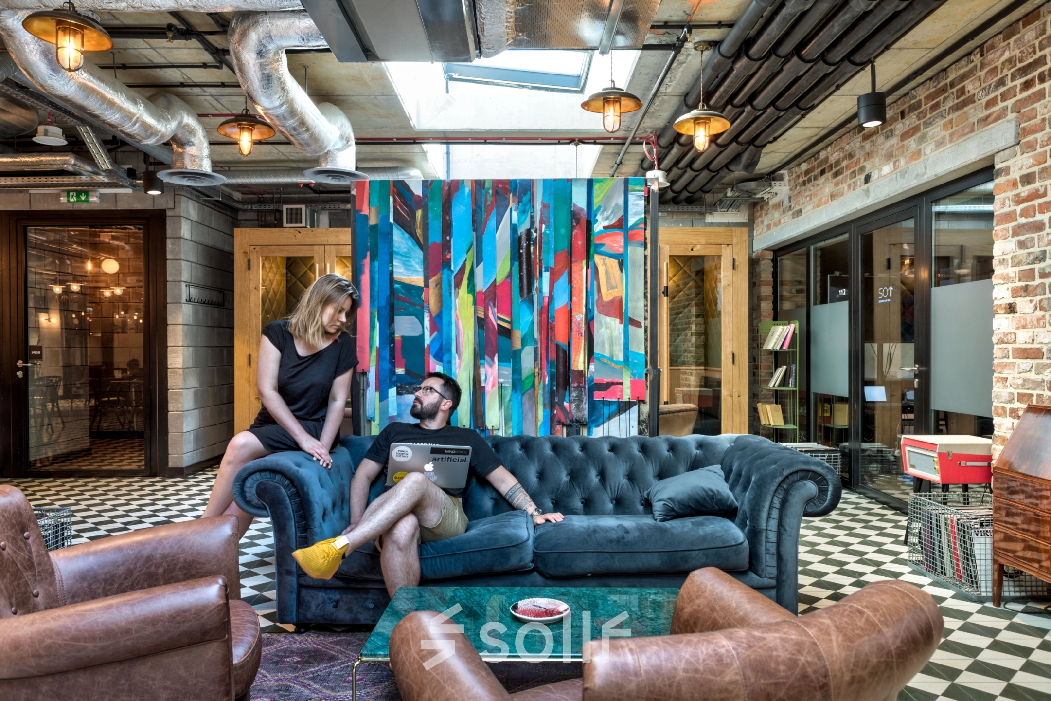 A vibrant office space with colorful decor at Koszykowa 61, Warsaw Śródmieście. Two people engage in discussion on a plush sofa. Ideal for rent office space with creative ambiance.