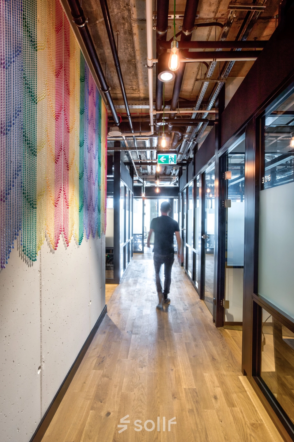 Man walks down a modern office hallway in Koszykowa 65, Warsaw Śródmieście, featuring colorful wall art and industrial design, perfect for office space rental.