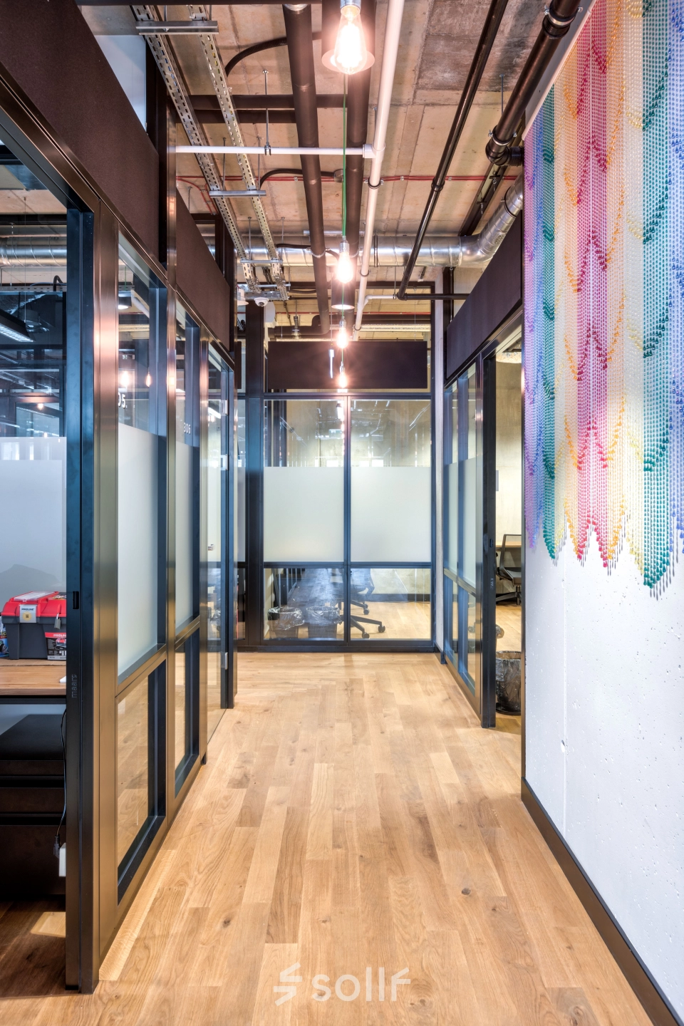 A bright, modern office hallway with glass partitions and a colorful wall mural at Koszykowa 65, perfect for office space rental in Warsaw Śródmieście.