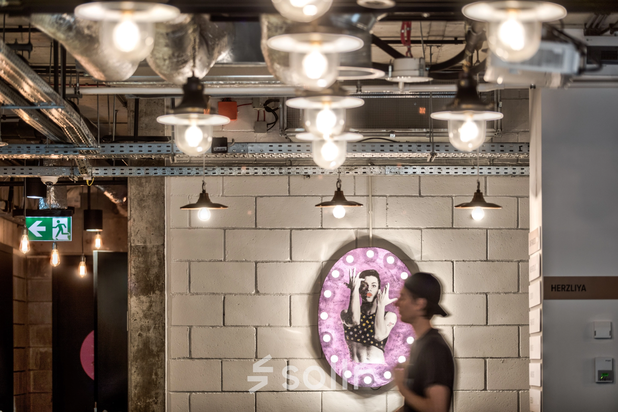 Modern office space at Koszykowa 65 in Warsaw Śródmieście, featuring ambient lighting and a unique wall decoration. A person is seen walking through the area.