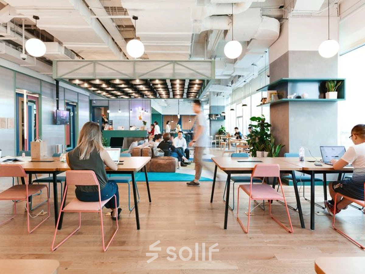 Modern office space rental at Krakowskie Przedmieście 13, Warsaw Śródmieście, featuring furnished open workspaces with people working on laptops, vibrant lighting, and a lounge area in the background.