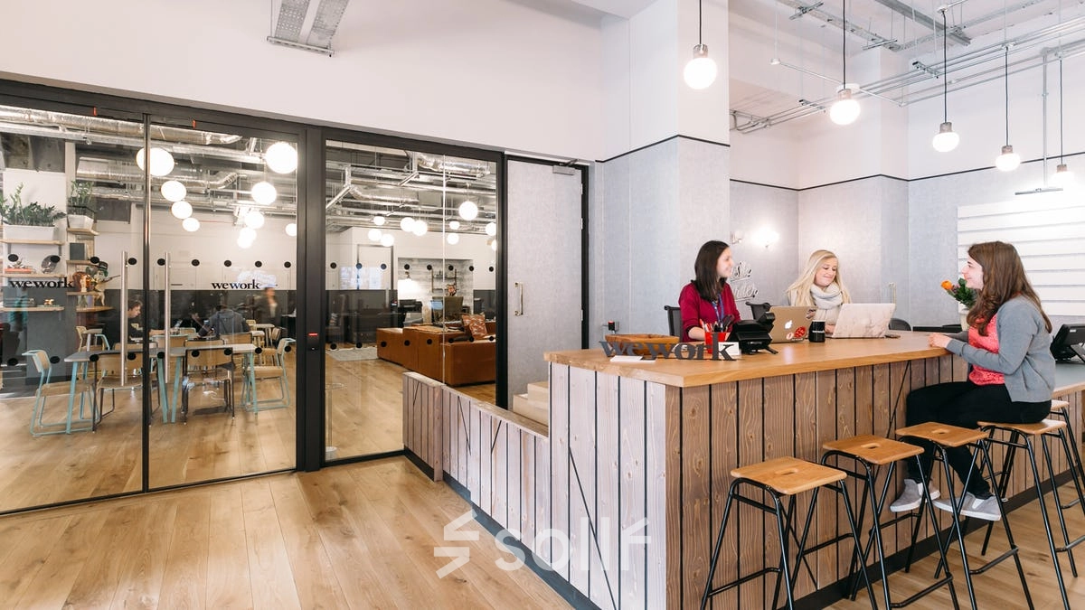 Inside an office space rental at Krakowskie Przedmieście 13, Warsaw Śródmieście, featuring a reception area with wooden seating and three people discussing work.