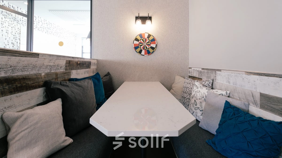 Cozy office space with a long table surrounded by cushioned seating and modern decor, ideal for casual meetings or breaks. Perfect for those seeking office space rental in the heart of Warsaw Śródmieście.
