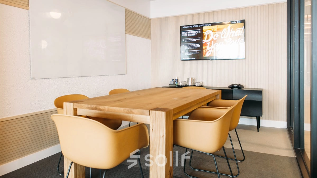 Furnished office space at Krakowskie Przedmieście 13 in Warsaw Śródmieście, featuring a wooden table and yellow chairs under a wall-mounted screen, ideal for office space rental.