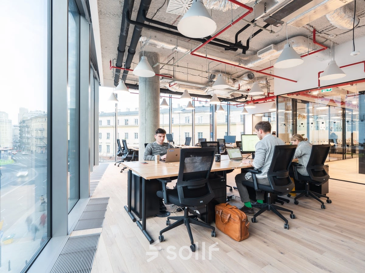 Modern workspace at Krucza 50, Warsaw Śródmieście, featuring large windows and professionals engaged in business activities. Ideal office space rental opportunity with sleek interiors.