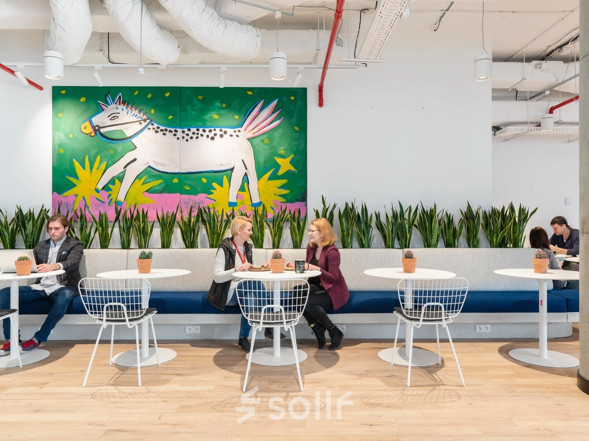 People engaged in discussion at tables in a stylish, furnished office space with vibrant wall art at Krucza 50, ideal for office space rental in Warsaw Śródmieście.
