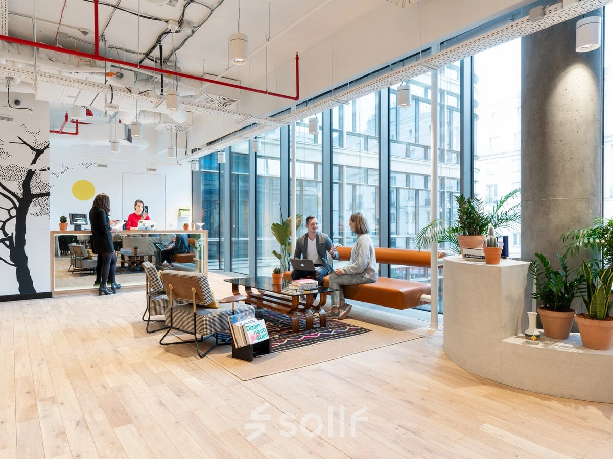 Modern office space at Krucza 50, Warsaw Śródmieście, featuring open seating areas with people engaged in conversation and light work. Ideal for office space rental.