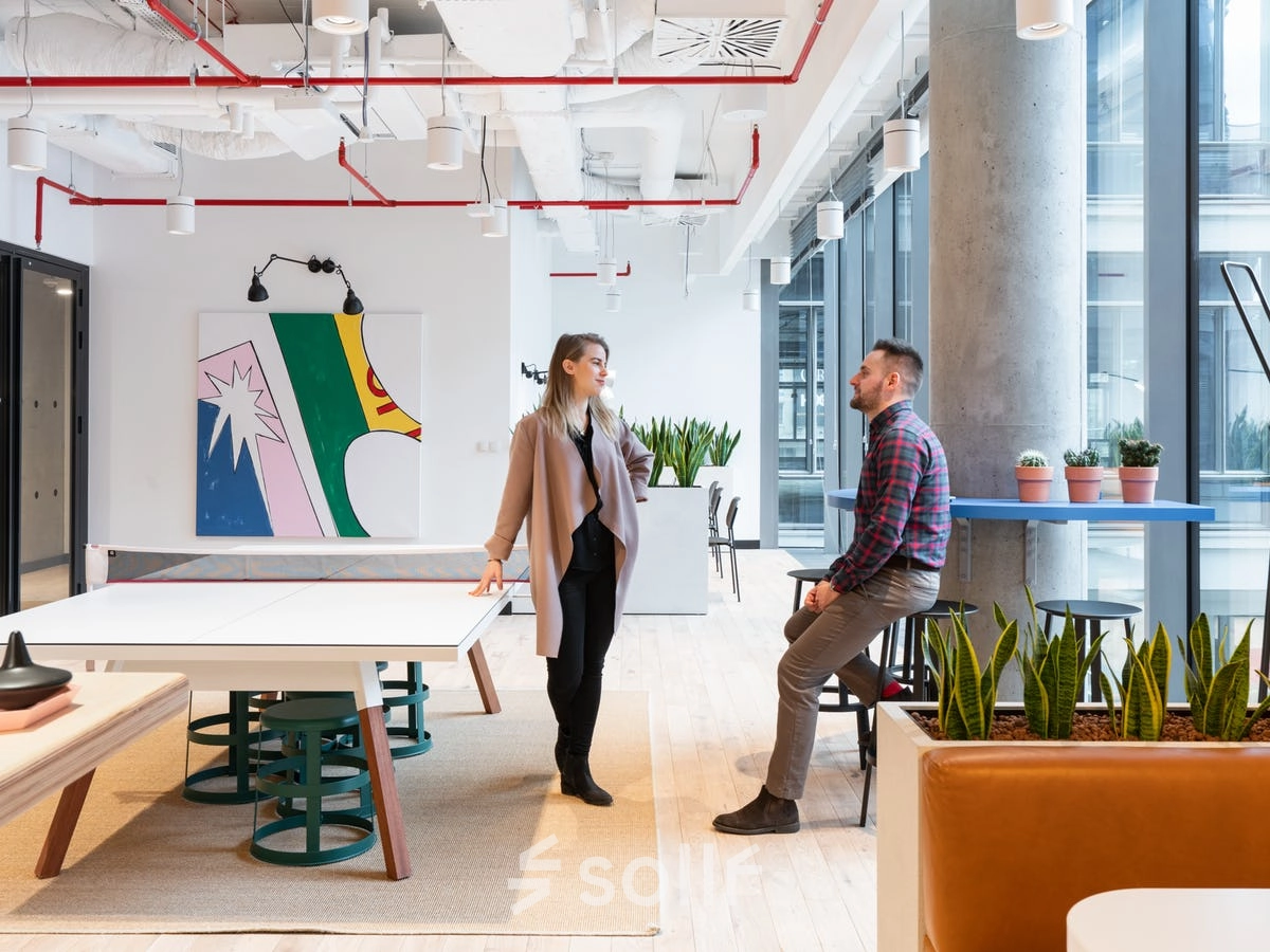 Office space at Krucza 50 in Warsaw Śródmieście with modern decor and plants. Two people discuss business near a table.