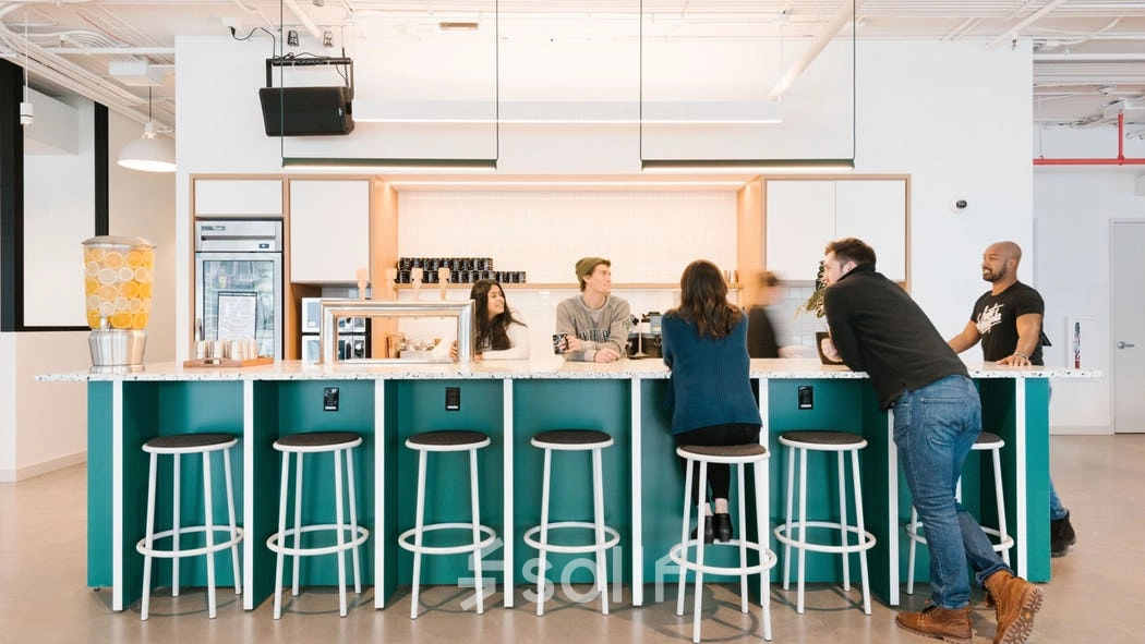 Modern office space with a group of people engaged in a casual meeting around a bar-style counter, perfect for office space rental in Warsaw Wola.