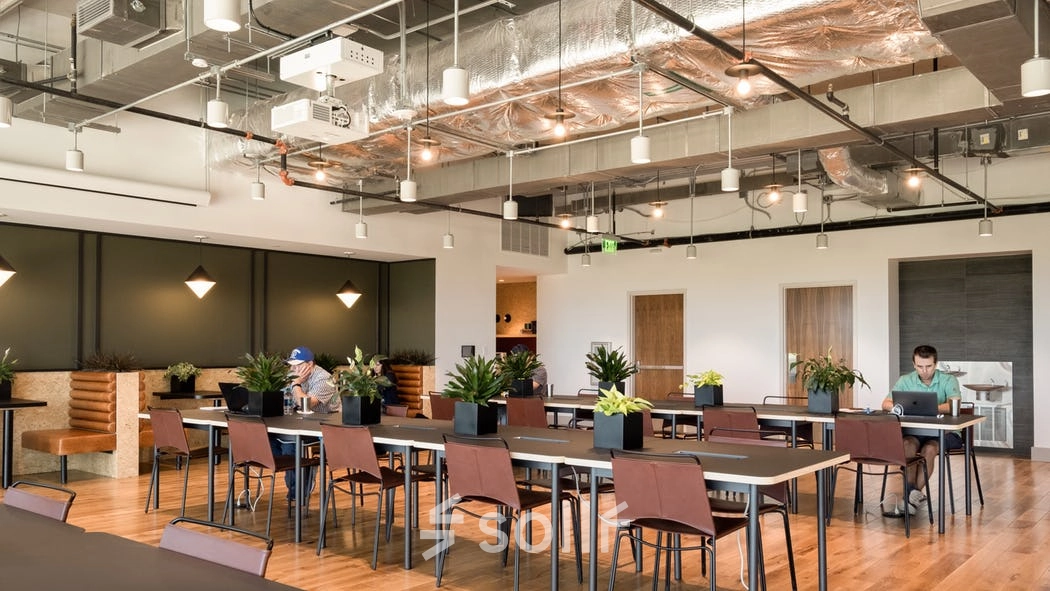 Modern office space rental in Warsaw Wola at Grzybowska 60 featuring open workspaces with stylish lighting and plants, two individuals working at separate tables.