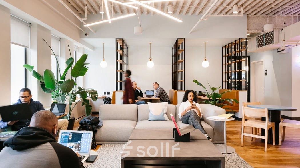 Modern office space at Grzybowska 60 in Warsaw Wola, featuring a comfortable lounge with people engaged in business tasks. Ideal for anyone looking to rent office space.