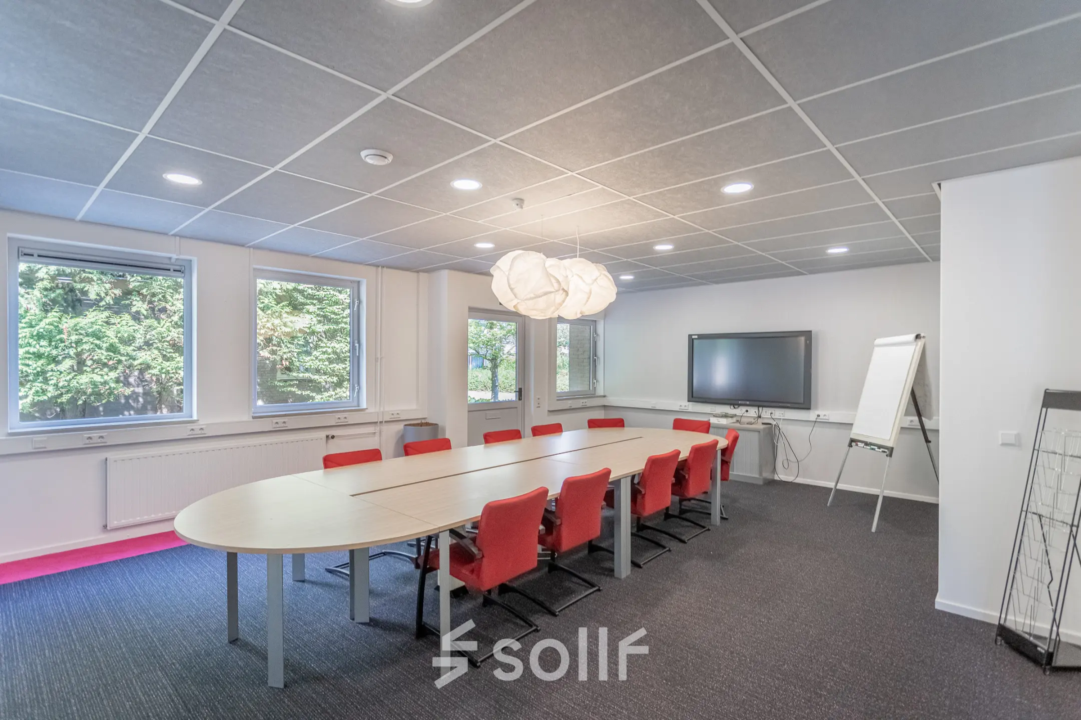 Modern conference room at Molenweer 2, Wateringen, available for office space rental with a large table, red chairs, smart board, and natural lighting.