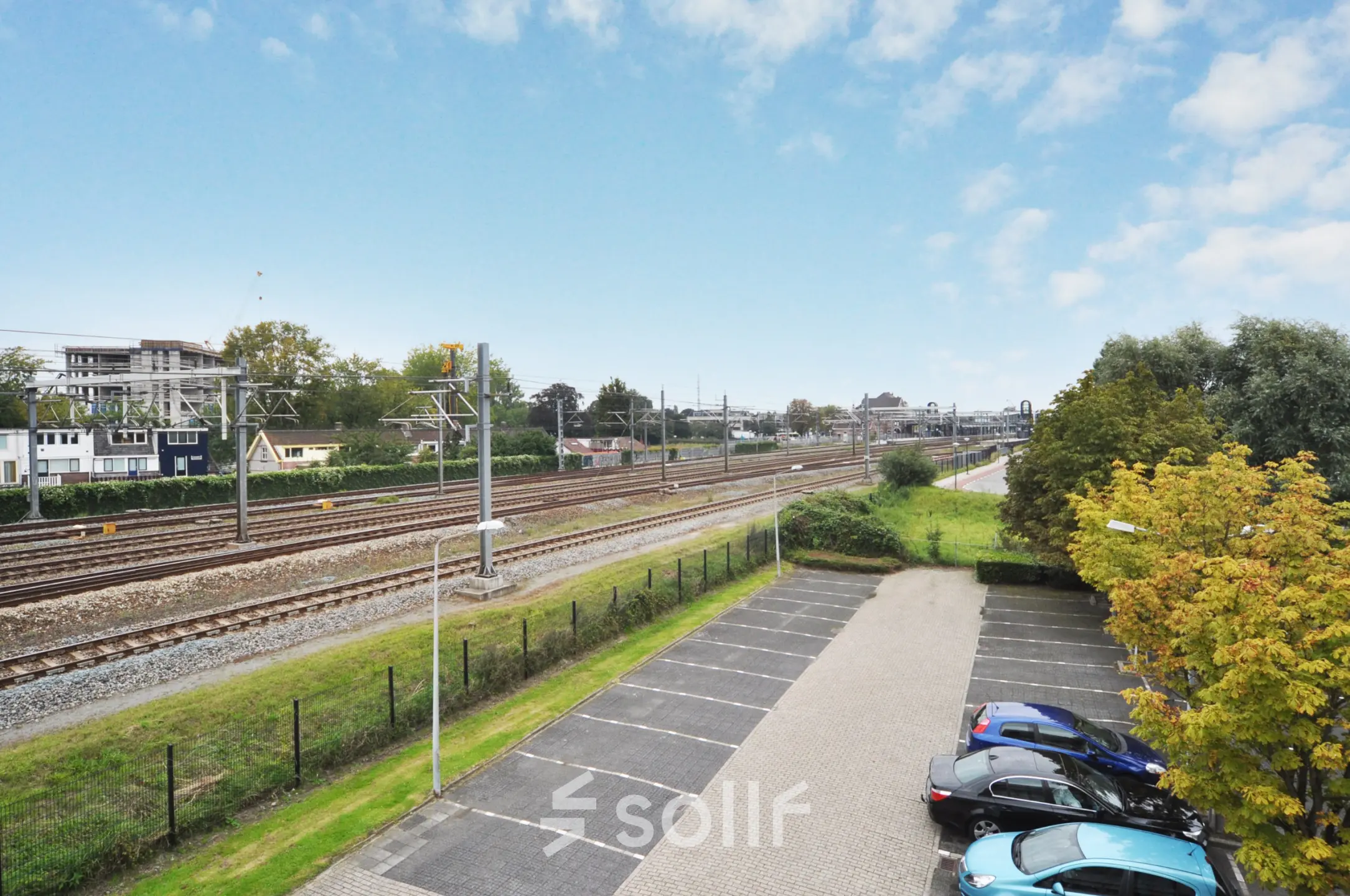 A view of the parking area and nearby railway tracks from Houttuinlaan 4, Woerden, ideal for nearby office space rental.
