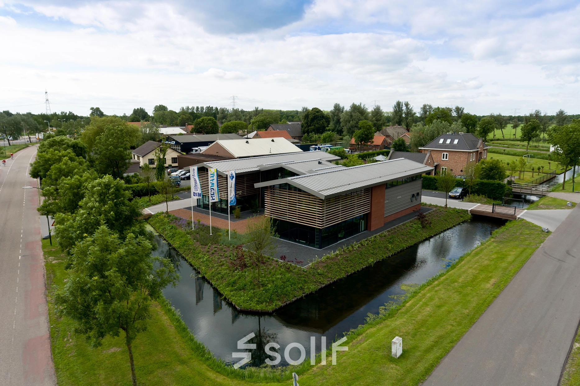 Aerial view of a modern office building for rent surrounded by greenery and a canal at M.A. Reinaldaweg 2d, Woerden. The architecture features sleek lines and a practical design, ideal for professional use.