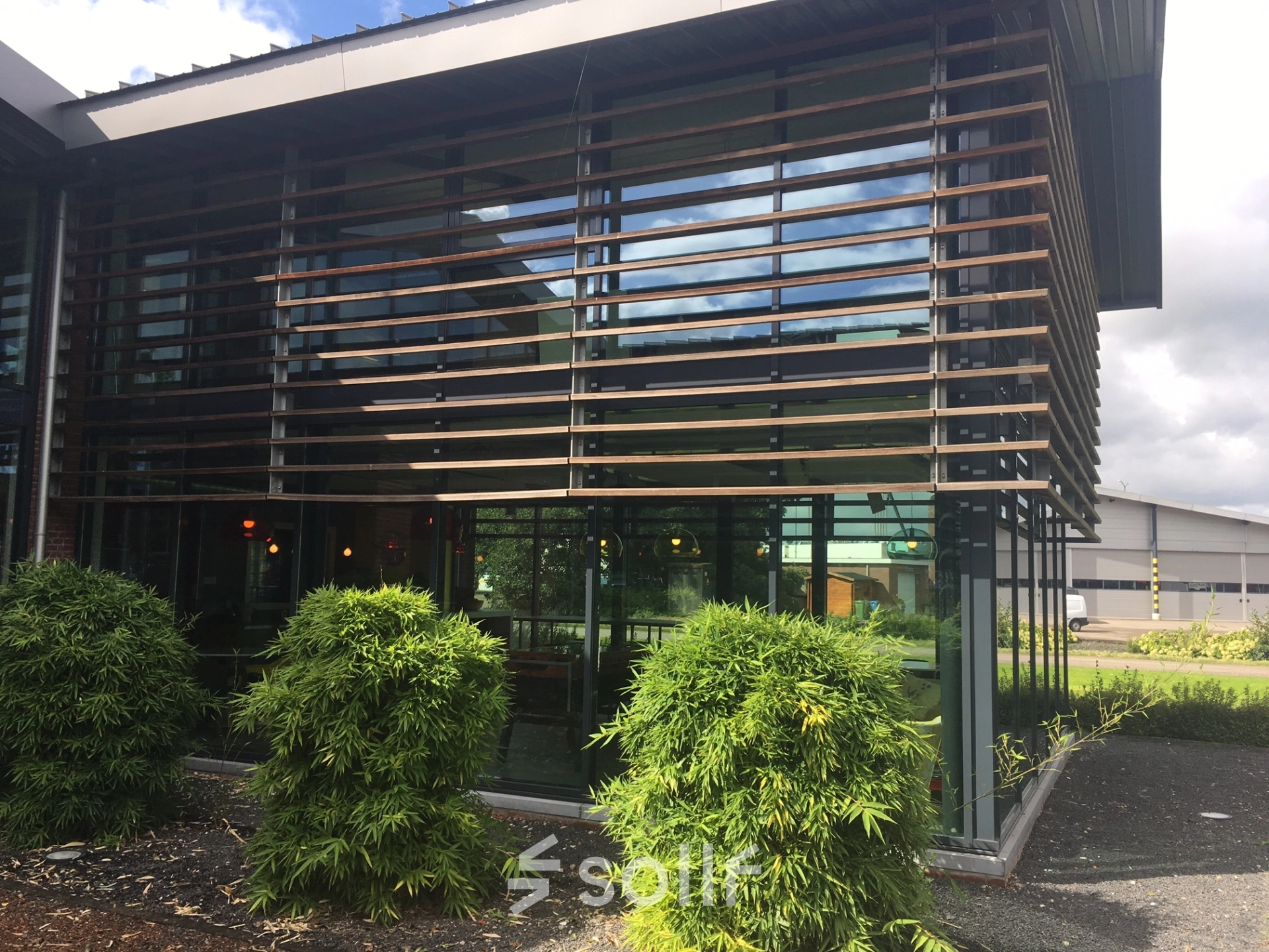 Exterior view of the office to rent at M.A. Reinaldaweg 2d in Woerden, featuring large glass windows and modern wooden slats, surrounded by greenery.
