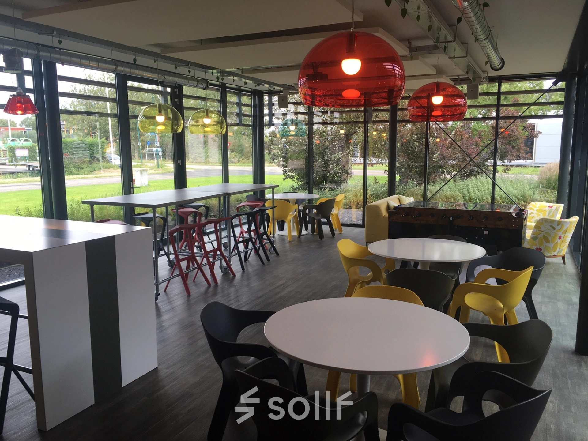 A modern, furnished office space with colorful seating and large windows in Woerden, ideal for rent office space seekers. The room is bright and versatile, featuring communal tables and comfortable chairs.