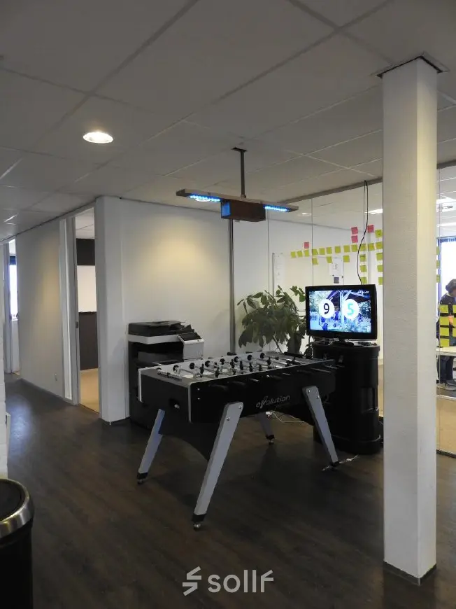 Office with a foosball table, TV displaying a sports score, and office equipment at Pompmolenlaan 9, Woerden, available for rent.
